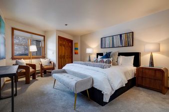 The bedroom at Chateau Chamonix CX114 features a king-sized bed with a dark headboard, white bedding, and colorful pillows, flanked by two table lamps on wooden nightstands.