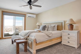 A cozy bedroom at Resort Plaza 5043 features a queen bed, rustic wooden furniture, and a balcony with snow-covered mountain views.