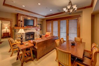 A living room with a fireplace, a large leather couch, a coffee table, and a dining table with chairs.