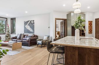 An inviting open-concept living room with a leather sofa, Christmas tree, and a modern kitchen island with bar stools.