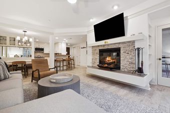 Modern open-concept living room with a glowing stone fireplace and view of the kitchen in The Charter C250.