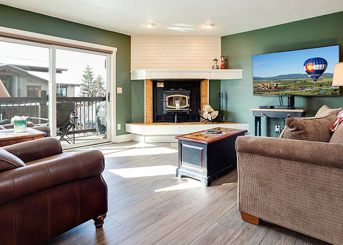 A cozy living room at Ranch at Steamboat RA107 with a fireplace, comfortable seating, a flat-screen TV, and access to a patio.