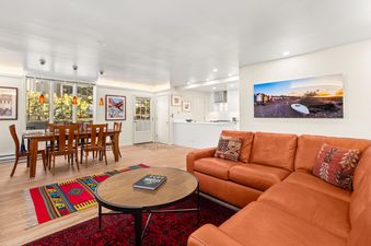 Living area of Chateau Dumont Unit 23 featuring an orange leather sectional sofa, a wooden dining table, and a glimpse of the kitchen.