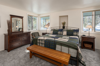 A cozy bedroom at Tamarack Townhomes 34 with a queen-size bed, dark wood furniture, and snow-dusted window views.