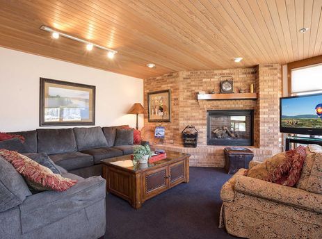 A cozy and inviting living room at Chateau Chamonix CX134, featuring an L-shaped sofa, a wooden coffee table, a brick fireplace, and a large flat-screen TV.