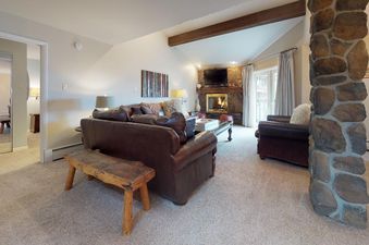 The comfortable and stylish living room in Westwind 402 is furnished with brown leather sofas, a wooden bench, a stone fireplace, and a flat-screen TV.
