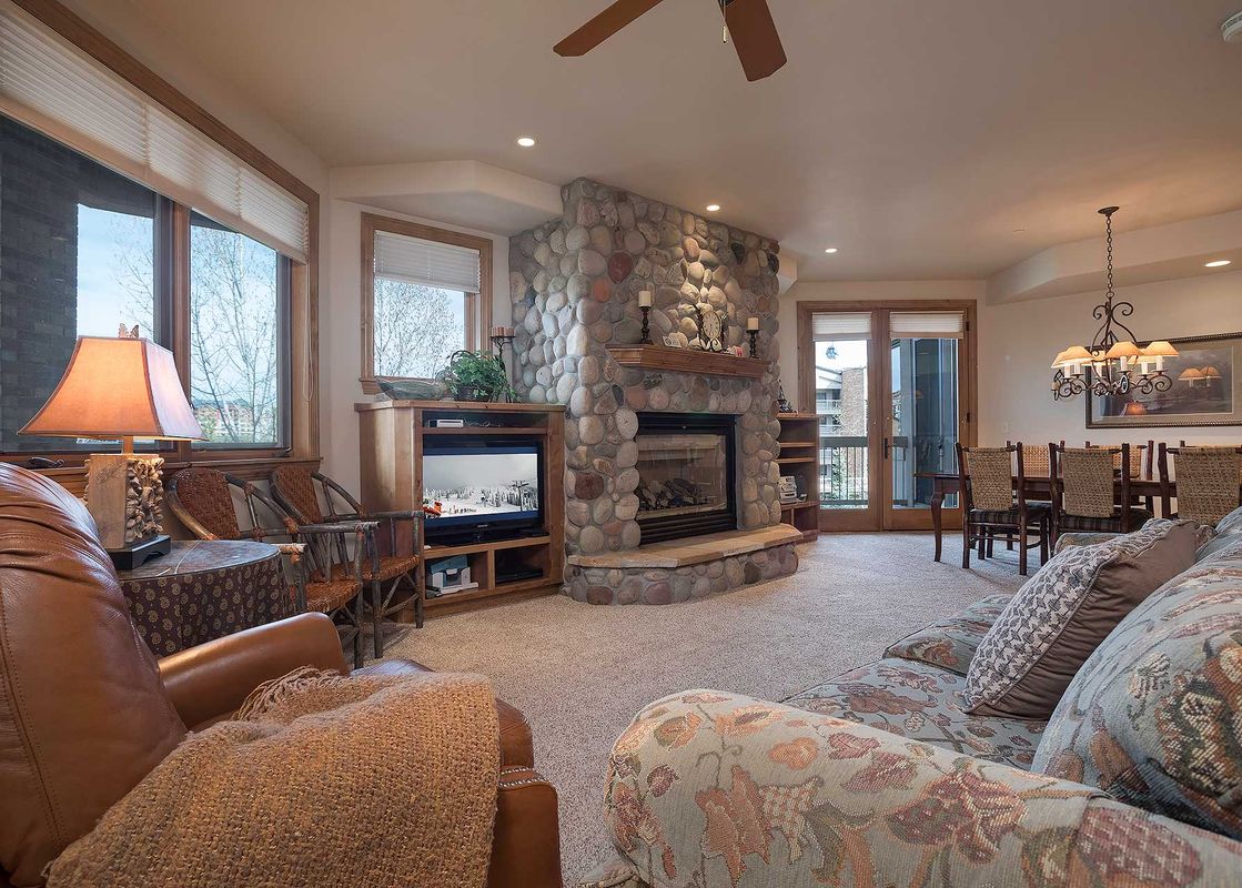 A cozy living room in Chateau Chamonix CX333 with a large stone fireplace, comfortable seating, and a dining area in the background.