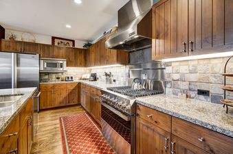 A gourmet kitchen at Snow Cloud Lodge 715 featuring wooden cabinetry, stainless steel appliances, granite countertops, and a large gas range.