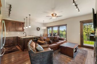 An inviting open-concept living room and kitchen in Landing Unit A, featuring a comfortable leather sofa, a well-equipped kitchen with dark wood cabinetry, and large windows offering scenic outdoor views.