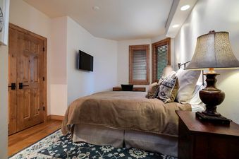 A cozy bedroom at Chateau Chamonix CX342 features a bed with a brown duvet, wooden doors, a wall-mounted TV, and wooden blinds on the windows.