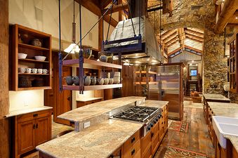 A rustic yet modern kitchen features a large island with a gas range, stainless steel appliances, and ample wooden cabinetry.