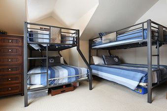Two bunk beds with blue and white striped bedding are neatly made in a bedroom with a sloped ceiling and light-colored carpet.