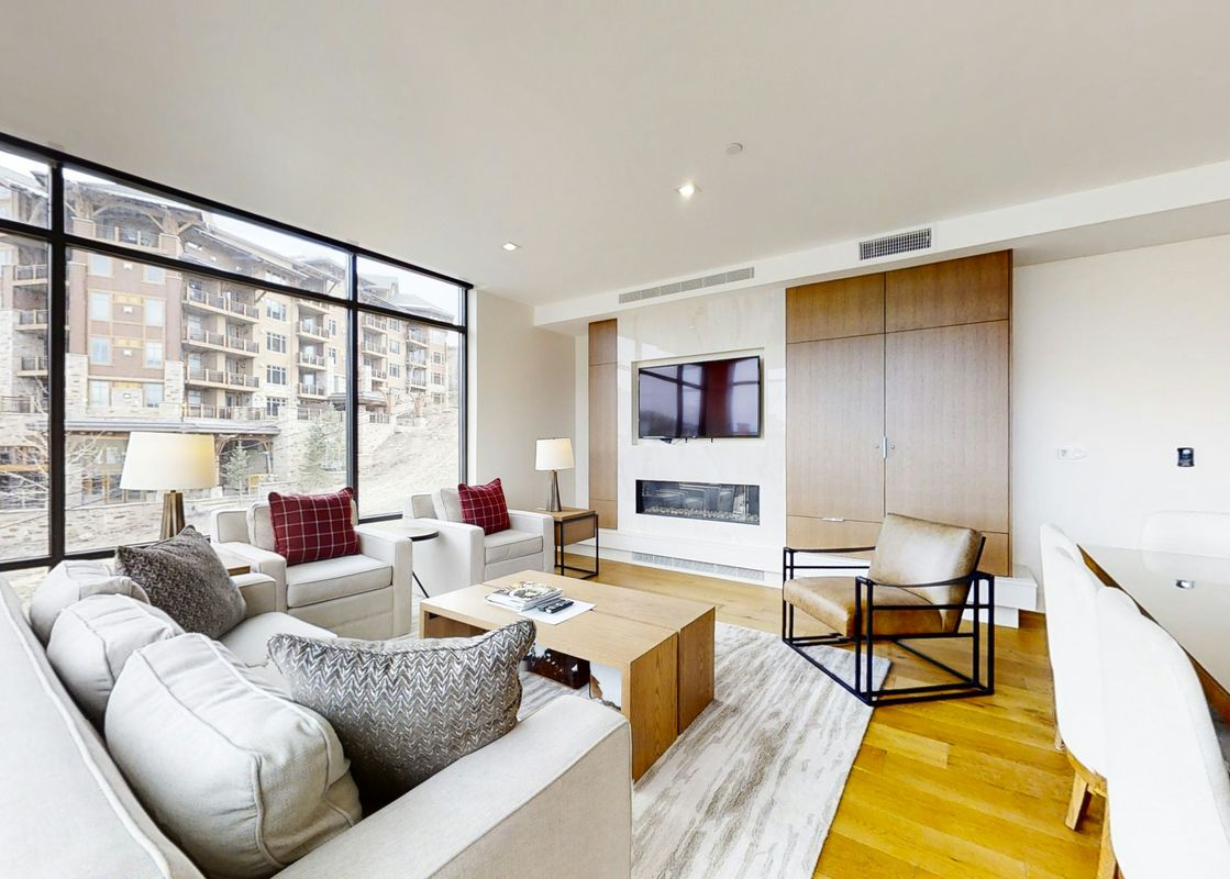 The Lift 402 features a large living area with a fireplace, a large flat-screen TV, and floor-to-ceiling windows showcasing a stunning mountain view.