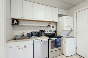 A fully equipped kitchen with white cabinets, granite countertops, stainless steel appliances, and a stacked washer and dryer.