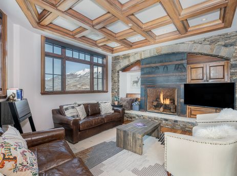 A cozy living room with a lit fireplace, leather sofas, and a large window offering a view of snow-capped mountains.
