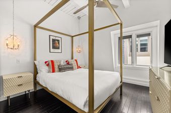 A luxurious bedroom at Chateau Dumont Unit 21 with a gold four-poster bed, white linens, patterned pillows, a cream nightstand, and a crystal chandelier.