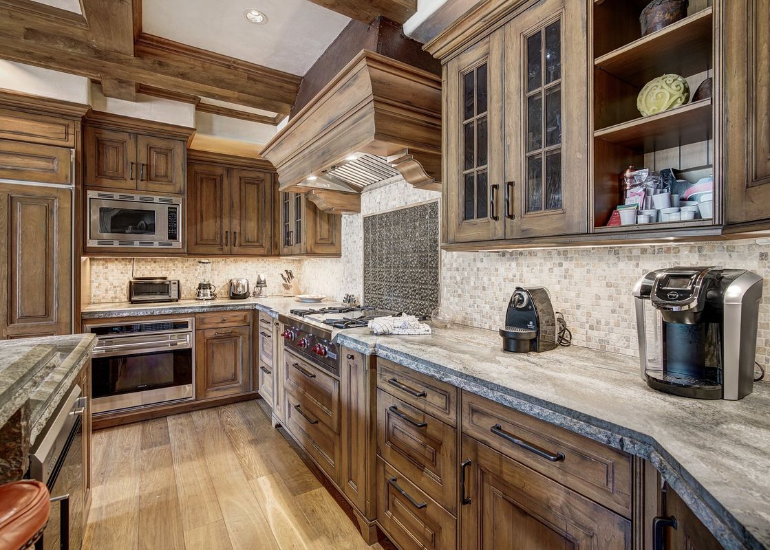 A spacious kitchen with rich wooden cabinetry, stone countertops, and modern stainless steel appliances.