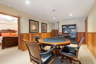 A dedicated games room within the Lake View Escape, featuring a large octagonal wooden table surrounded by four upholstered chairs, with a glimpse of a comfortable bedroom through an open doorway.