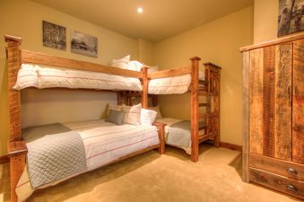 A cozy bedroom in Cowboy Heaven Luxury Suite Unit 2B features a wooden bunk bed with white and red striped bedding, light yellow walls with rustic art, and a wooden wardrobe on light brown carpet.