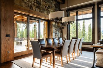 The dining room at 7 Renegade Rd Moonlight Basin Lodging has a large wooden table with six chairs, and a window with a view of the forest.
