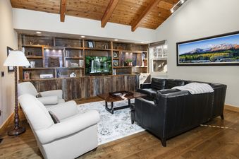 Cozy living room in Buffalo Park 3 with a vaulted wood ceiling, black leather sofa, two light grey armchairs, and a large built-in shelving unit with a TV.