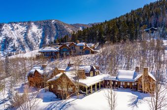 A drone shot captures the Five Trees Estate, a collection of snow-dusted luxury homes on a mountain slope, under a brilliant blue sky.