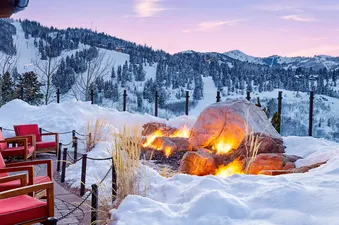 A fire pit on a snowy patio with a view of snow-covered mountains in the distance.