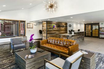 A large brown leather couch and two grey armchairs arranged around a coffee table, with a reception desk and decorative wood paneling in the background, create a welcoming atmosphere in Torian Plum Plaza 202.