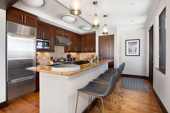 The kitchen in Lumiere Three Bedroom Penthouse features a modern design with stainless steel appliances, granite countertops, and a breakfast bar with four stools.