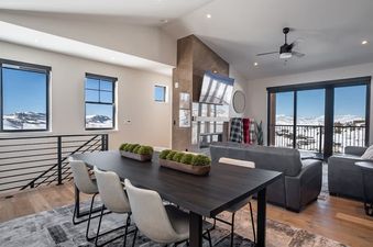 The dining area and living room of the Penthouse in the Pines feature modern furnishings, a fireplace, and large windows offering panoramic mountain views.