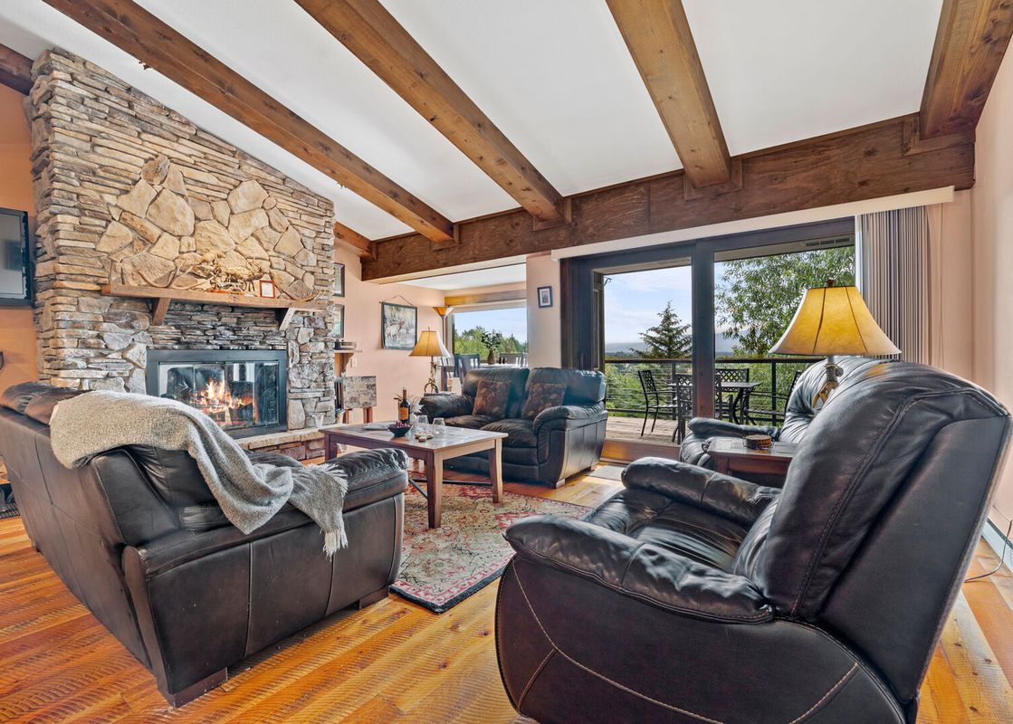 Cozy living room in Snowridge 6 with a stone fireplace, leather seating, and mountain views.