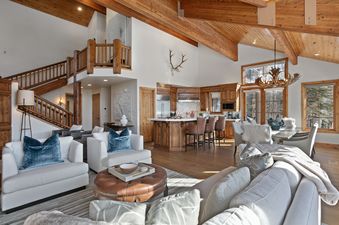 The spacious main living area of the Bellemont 5 with vaulted wooden ceilings, a comfortable lounge, a fully equipped kitchen, and a dining area with an antler chandelier.