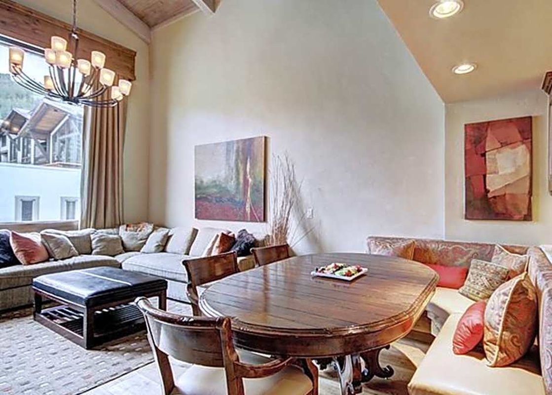 The dining area and living room of The Lodge at Vail 3 Bedroom Residence features a large wooden dining table, a cozy sectional sofa, and a stunning view of the surrounding landscape.
