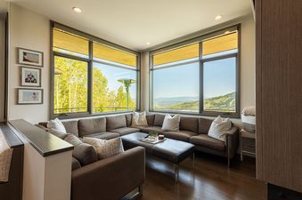 A modern lounge area at Park City Colony Obsidian Ridge with a large sectional sofa, hardwood floors, and expansive windows offering scenic mountain views.