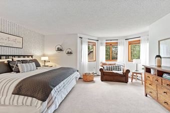 A bedroom with a king-size bed, a large window with a view of the forest, and a sitting area with a chair and a coffee table.