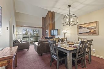 A spacious living and dining area in Snow Flower 127 with a wooden dining table, leather sofas, a fireplace, and a balcony with an outdoor view.