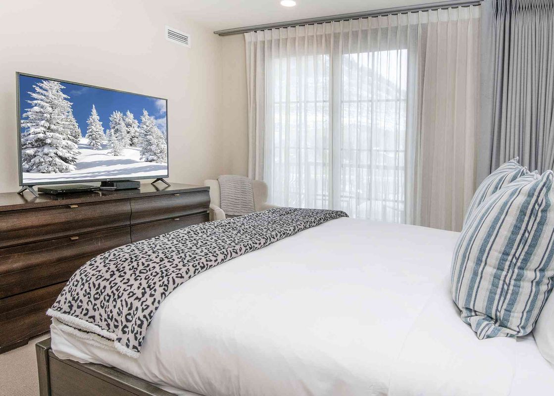 A bedroom in Ritz Carlton Vail 402 with a large flat-screen TV and a king-size bed with white linens and a leopard print throw.