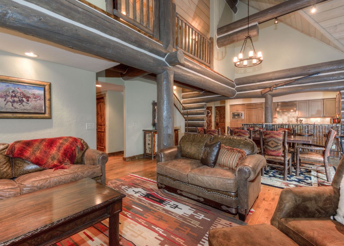 A wide view of Powder Ridge Cabin Manitou 1's living area, showcasing rustic decor, leather sofas, a wooden coffee table on a patterned rug, and exposed log beams.