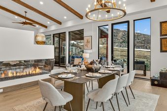 A luxurious dining room in The Duet Grande with a long dining table, modern chandelier, linear fireplace, and expansive windows showcasing mountain views.