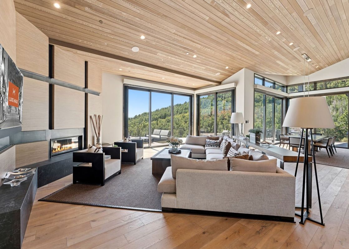 A modern living room with a large sectional sofa, a sleek fireplace, and floor-to-ceiling windows offering panoramic mountain views.