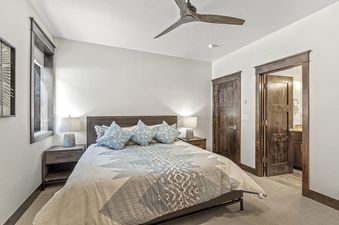 A bedroom with a king sized bed, a ceiling fan, and a lamp on the nightstand.