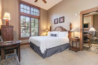 A hotel room with a king-size bed, two nightstands with lamps, a wooden dresser, and a large window.