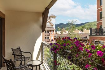 The private balcony of Montaneros 321 offers seating amidst colorful flowers with a view of mountains and village buildings.