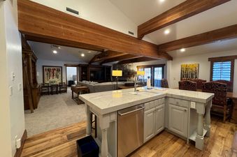 A spacious open-concept living area with a kitchen island, dining table, and living room, featuring rustic wood beams and cozy furnishings.