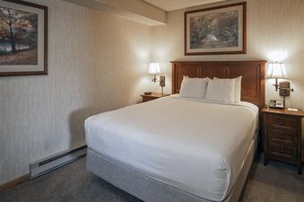 A cozy king bedroom at Colorado Suite Beaver Run Resort with white linens, wooden nightstands, and framed artwork.
