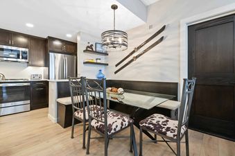 A modern kitchen and dining area at The Charter A2505 with dark wood cabinets, stainless steel appliances, a glass-top table, and chairs with cowhide cushions, all under a decorative chandelier.