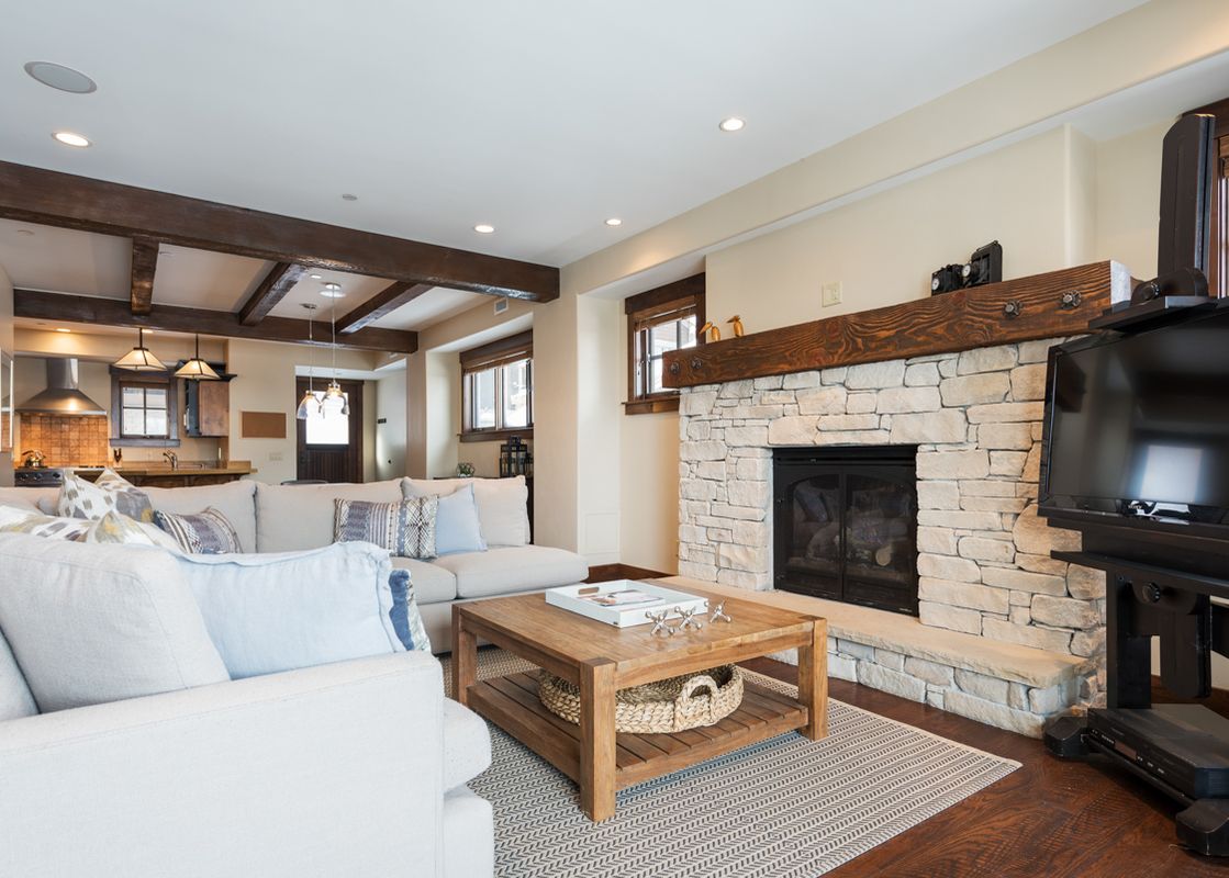 A spacious living area at Silver Star 404, featuring a light-colored sectional sofa, a rustic wooden coffee table, a stone fireplace, and a television, with a view of the kitchen and dining area in the background.