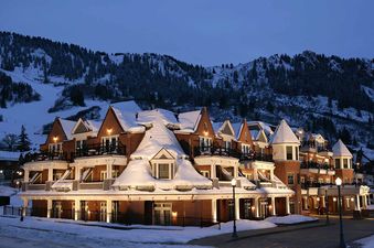 The Hyatt Lodge Room is nestled at the base of a snow-covered mountain, illuminated by warm lights at dusk.