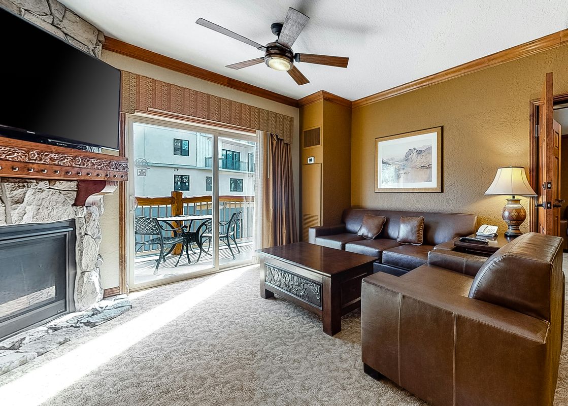 The living room of Westgate Iconic Condo 4814 features a stone fireplace, a comfortable leather couch, and a coffee table. The unit has large windows offering scenic views.