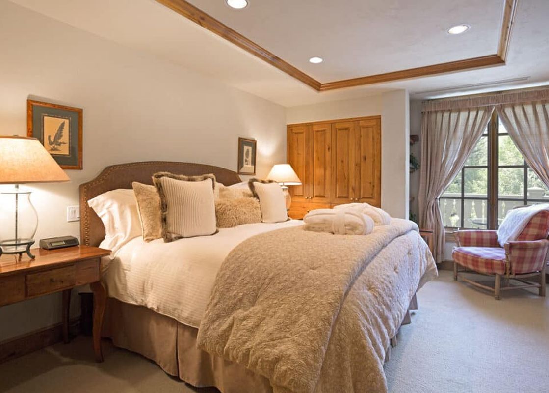 The master bedroom at Chateau Beaver Creek Residence 206 features a king-sized bed, a cozy armchair, and elegant wooden furnishings.